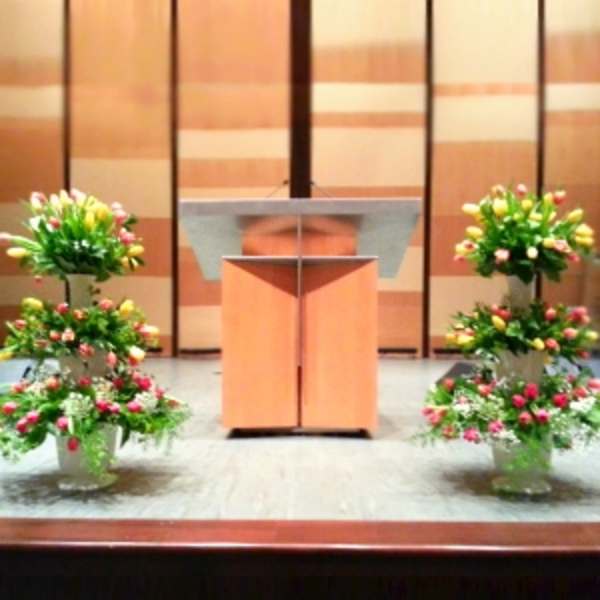 Four tiered floral arrangements flank a podium on a stage
