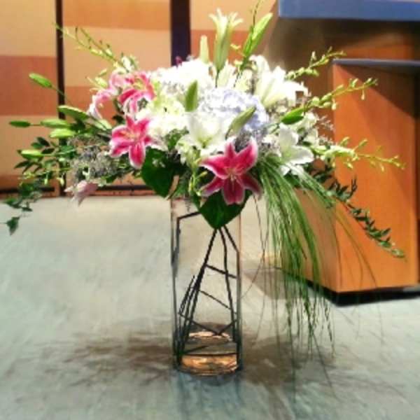 Tall floral arrangement with pink and white lilies in a metal stand
