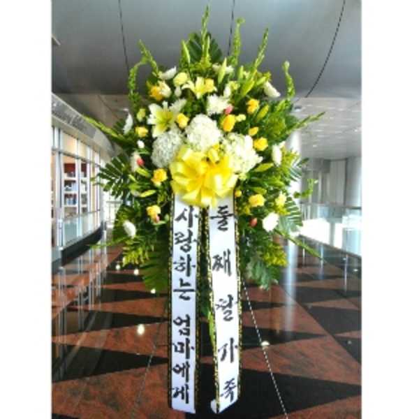 Tall standing spray of yellow and white flowers with large yellow bow and vertical message ribbons