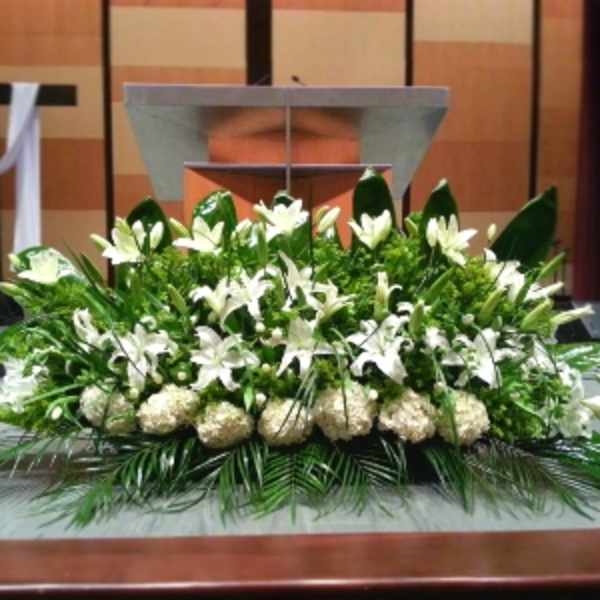 Low, elongated white lily and hydrangea arrangement on a stage in front of a podium