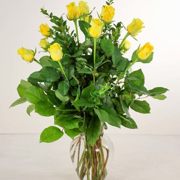 Yellow roses in a clear glass vase with dense green foliage