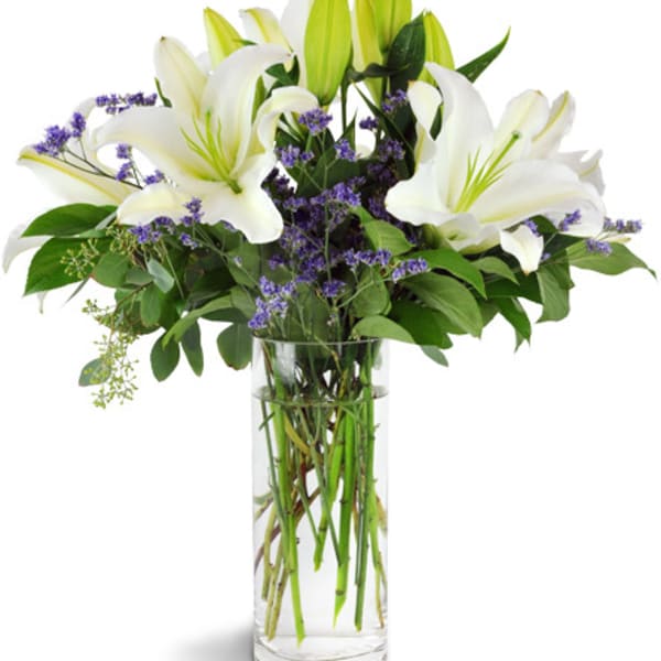 White lilies and purple filler flowers in a clear glass vase