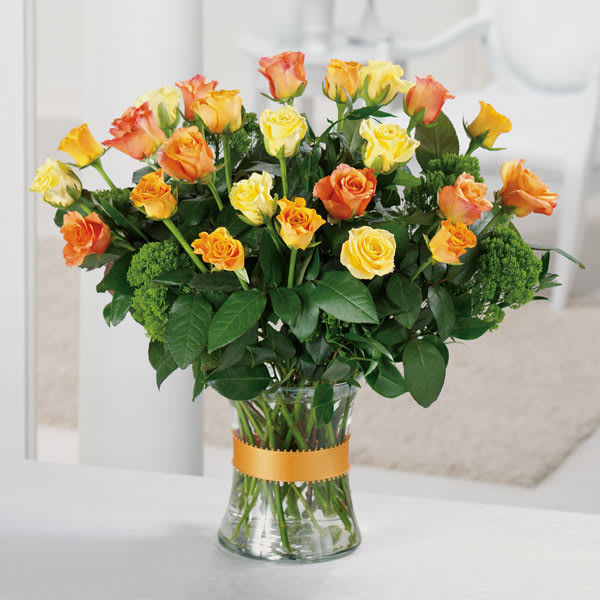 Yellow and orange roses in a clear glass vase with a ribbon band.