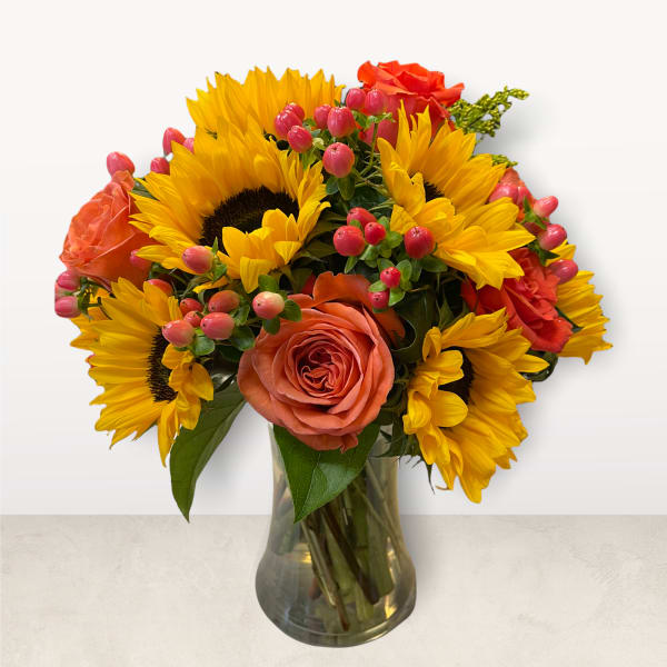 Bouquet of sunflowers and coral roses in a clear glass vase