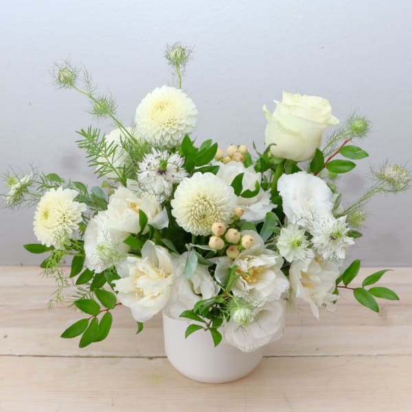 White floral arrangement in a white vase with roses and round blooms
