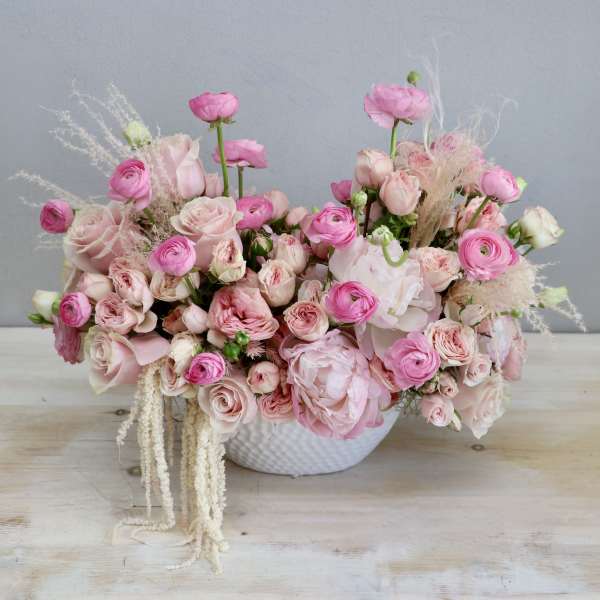 Low bowl arrangement of pink roses, ranunculus, and peonies in a white ceramic container