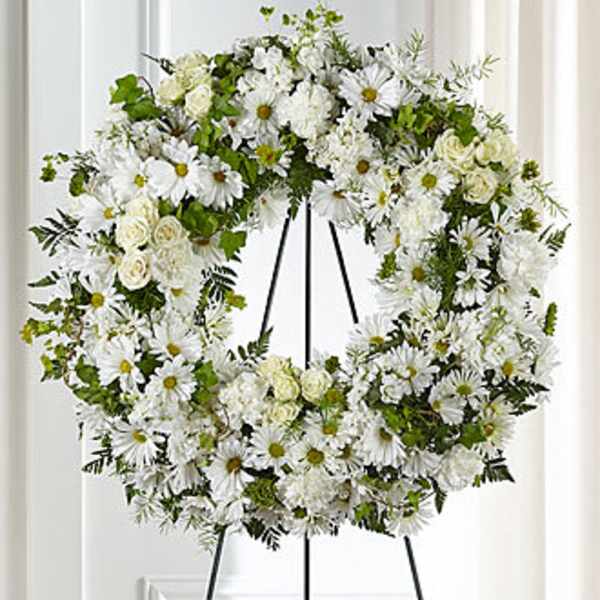 White floral wreath on a black stand with daisies and roses