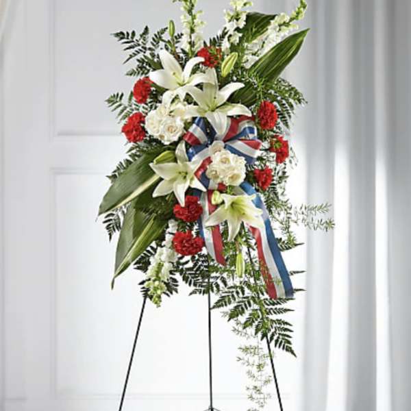 Standing floral spray with white lilies, red carnations, and ribbon on an easel