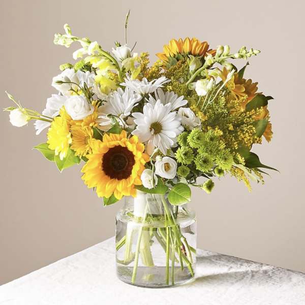 Bouquet of sunflowers, white daisies, and yellow flowers in a glass vase
