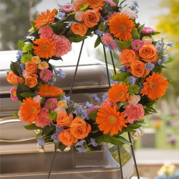 Orange and pink floral wreath on a stand in front of a casket