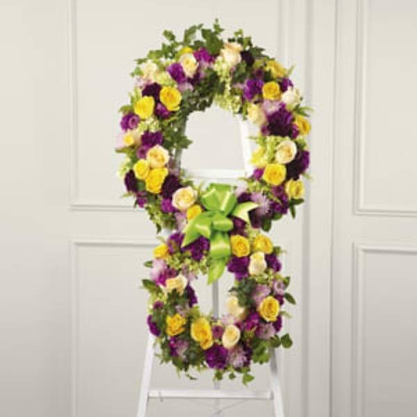 Purple, yellow, and white floral wreath on a white easel with a green bow