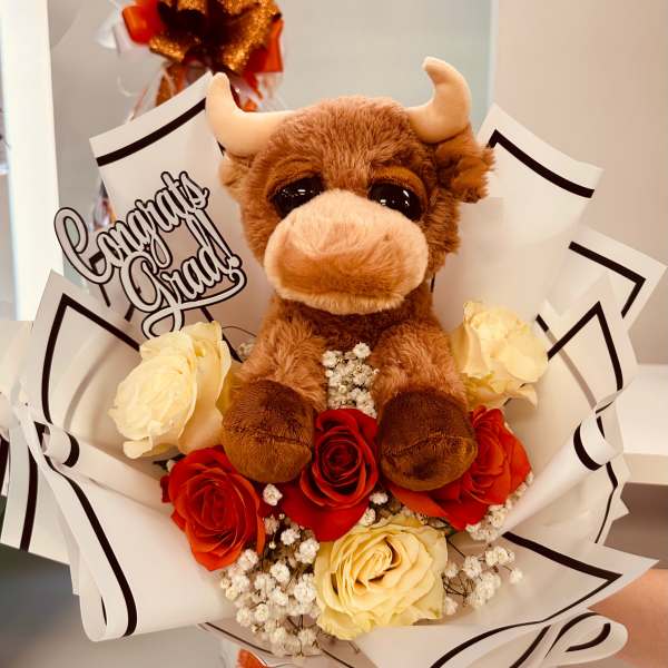 Bouquet with a plush bull toy, red and cream roses, and a Congrats Grad sign in white wrap.