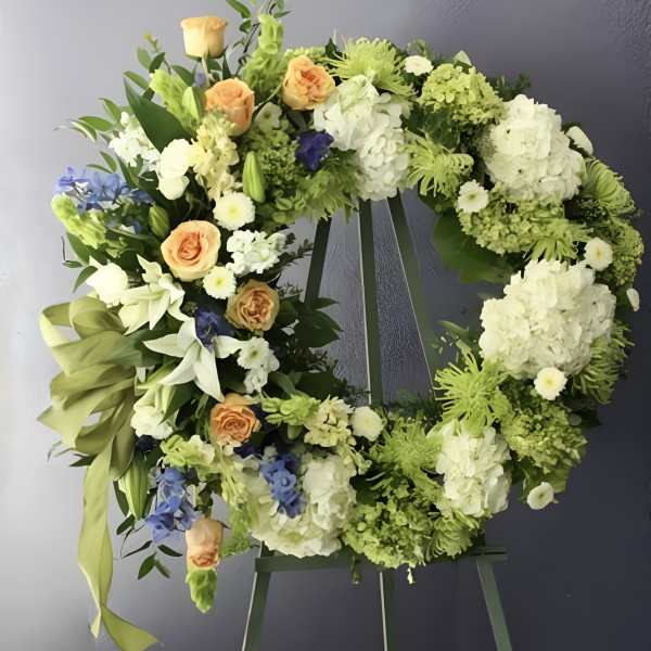 Circular floral wreath on an easel with white, green, peach, and blue flowers