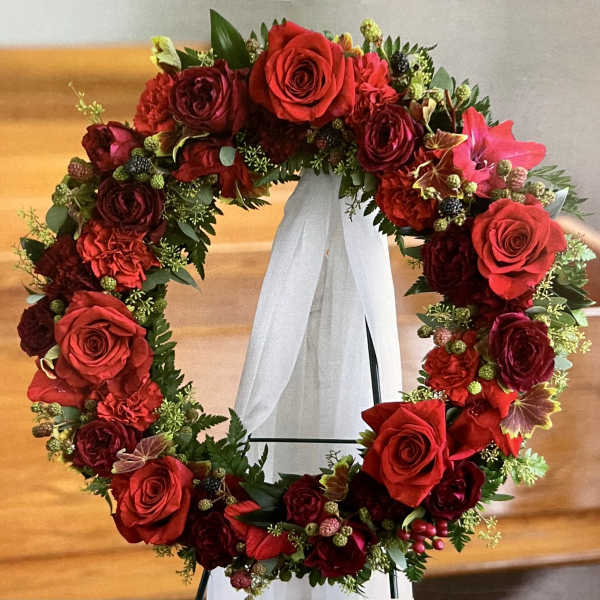 Red rose wreath on a white stand with a sheer ribbon