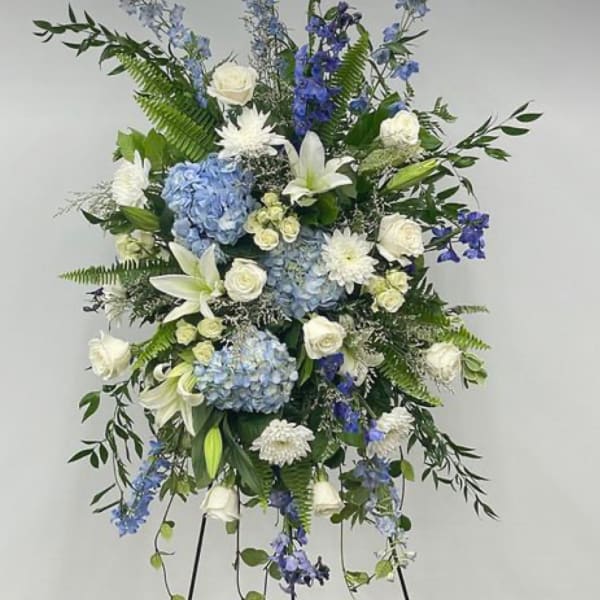 Standing floral spray with blue and white flowers on a black easel