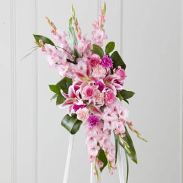 Pink floral spray with lilies and roses on a white stand