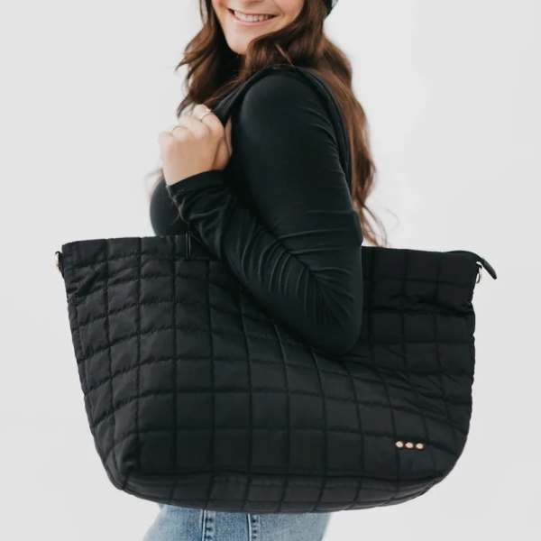 Woman carrying a large quilted black tote bag on her shoulder