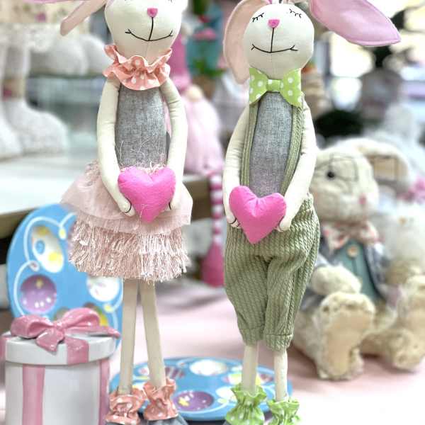Two plush bunny dolls holding pink hearts and wearing pastel outfits