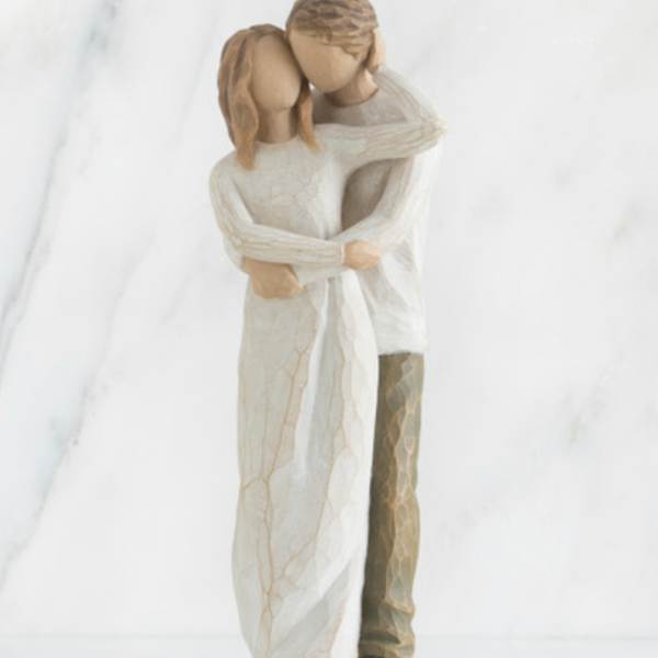 Two figurines embracing in cream-colored clothing