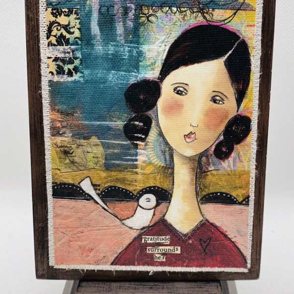 Framed mixed-media artwork of a girl with a bird and the words gratitude surrounds her