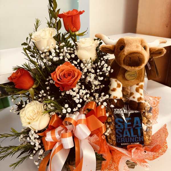 Basket with orange and white roses, baby’s breath, plush cow toy, and bag of sea salt popcorn.