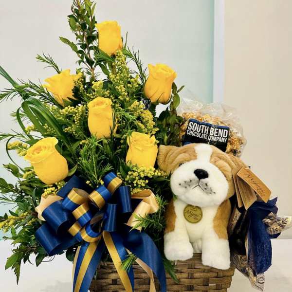 Gift basket with yellow roses, navy and gold bow, plush dog, and bagged chocolate snack