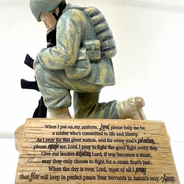 Soldier kneeling in prayer on a wooden plaque with engraved text