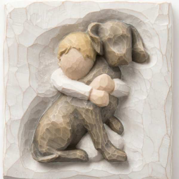 Ceramic relief of a child hugging a dog on a white plaque