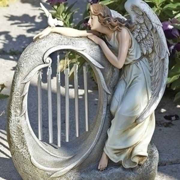 Angel statue leaning on a circular wind chime in a garden