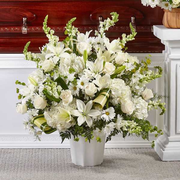 White funeral arrangement in a white vase with lilies, roses, and daisies