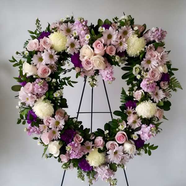 Heart-shaped floral wreath with pink and white flowers on a black stand