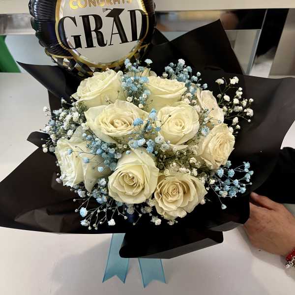 Graduation bouquet of white roses with blue and white filler flowers wrapped in black paper with a Congrats Grad balloon.