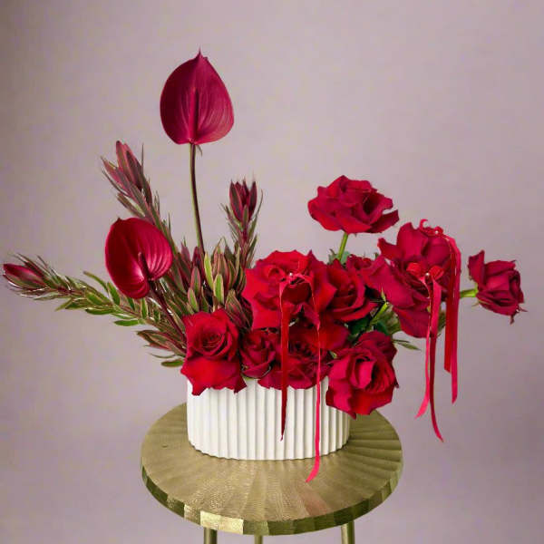 Red roses and burgundy anthuriums in a white ribbed vase