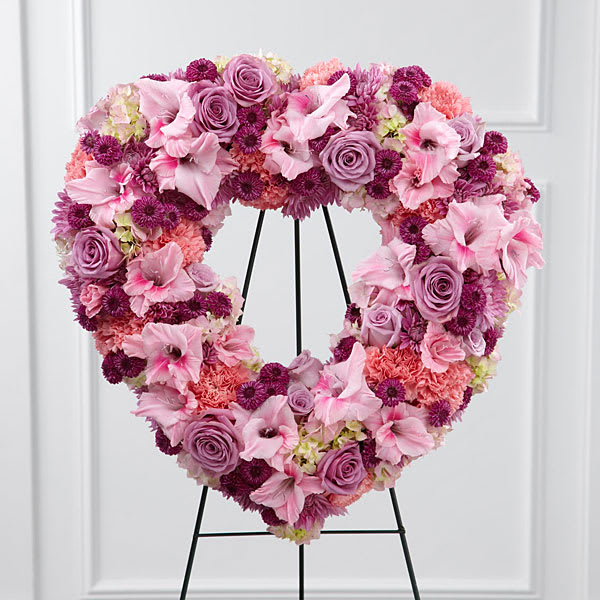 Heart-shaped floral wreath in pink and lavender tones on a black stand