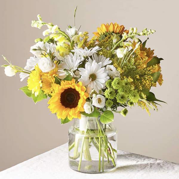 Bouquet of sunflowers, white daisies, and yellow blooms in a glass vase