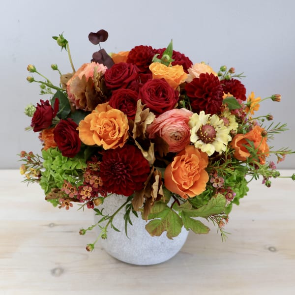 Low arrangement of red, orange, and yellow flowers in a white ceramic pot