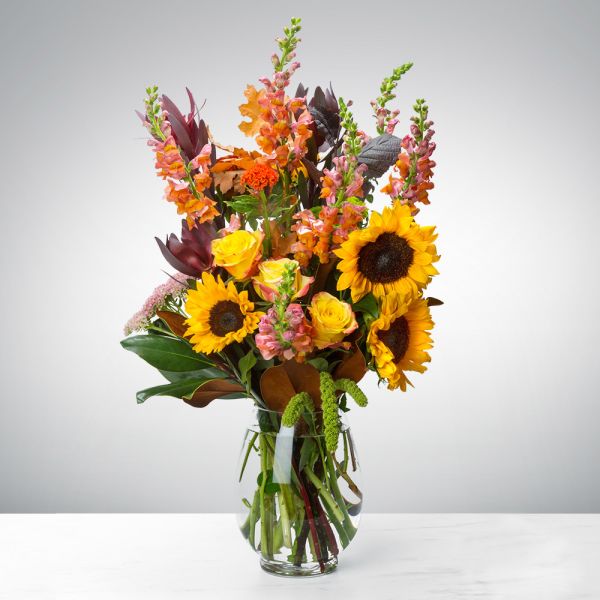 Tall bouquet of sunflowers and orange blooms in a clear glass vase