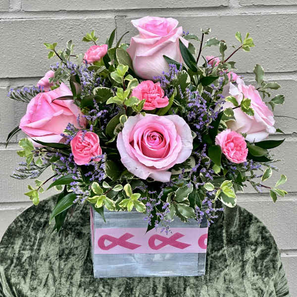 Pink roses and carnations in a square box with purple filler flowers.