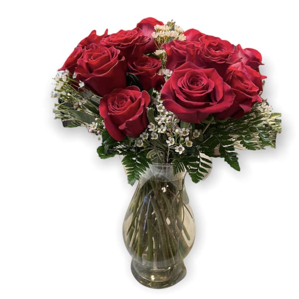 Red roses arranged in a clear glass vase with small white filler flowers