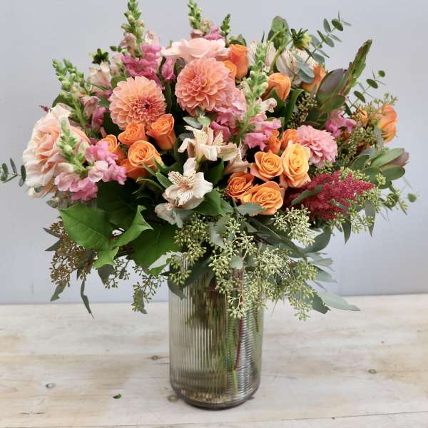 Tall mixed bouquet of pink and orange flowers in a ribbed glass vase