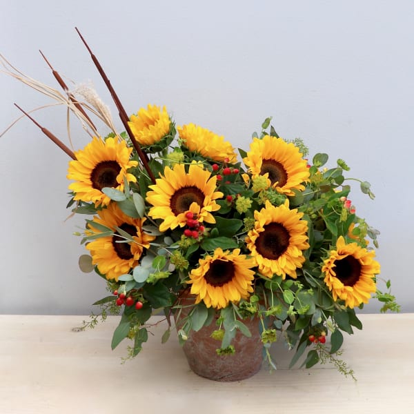 Asymmetrical arrangement of yellow sunflowers with red berries in a rustic pot