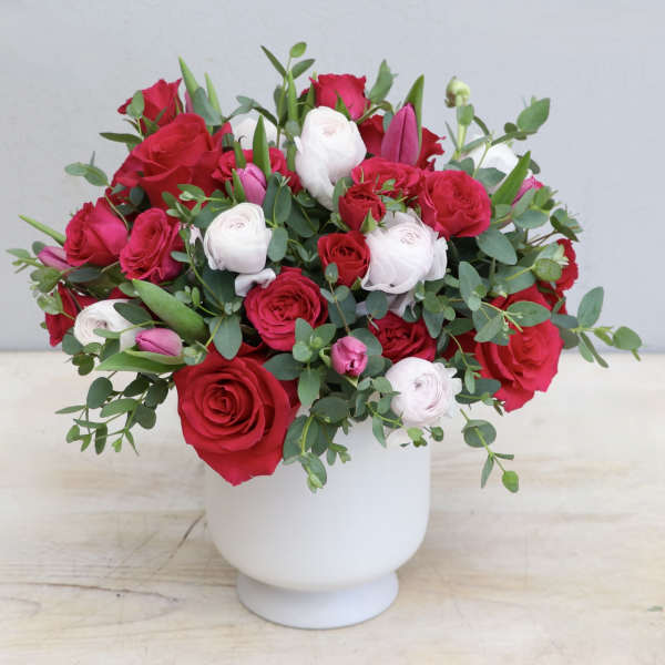 Red and white rose and ranunculus arrangement with pink accents in a white vase