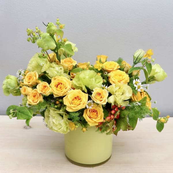 Yellow roses and pale green carnations arranged in a light green cylinder vase