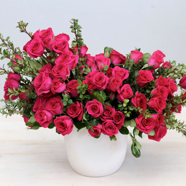 Lush arrangement of hot pink roses with green accents in a white ceramic pot