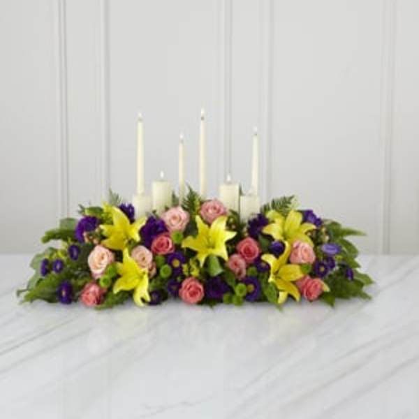 Low floral centerpiece with candles and pink, yellow, and purple blooms