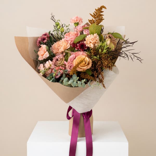 Bouquet of pink and peach flowers wrapped in brown paper with a purple ribbon