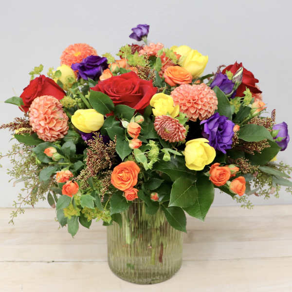 Mixed bouquet of roses, tulips, and dahlias in a glass vase