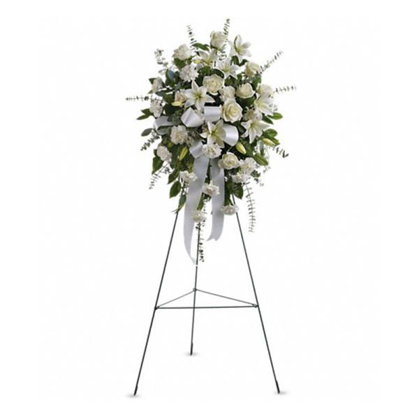 Tall white standing spray with roses, lilies, carnations, and ribbon on a metal easel.