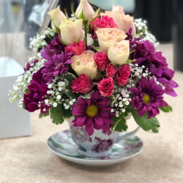 Bouquet of pink and cream roses with purple daisies in a floral teacup