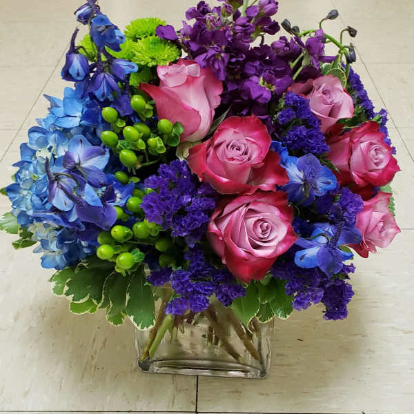 Bouquet of pink roses, blue and purple flowers in a clear glass vase